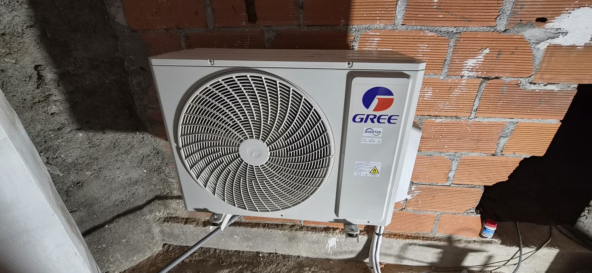 Unité extérieure Gree Inverter installée au sol contre mur en briques – M.T CLIM ELEC